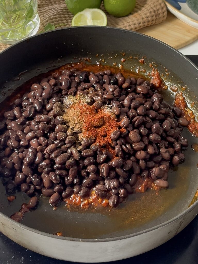 black beans and spices being added on top of the garlic and paste mixture