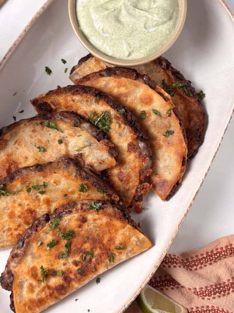 a plate of crispy black bean tacos topped with fresh cilantro, a dipping sauce just in the photo