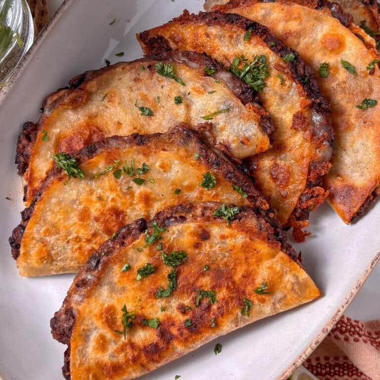 an overhead photo of crispy black bean tacos stacked on an oval plate, topped with fresh cilantro