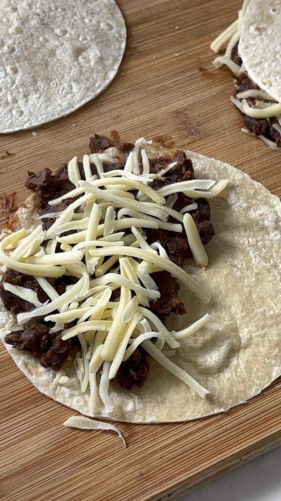 a black bean taco pre-cooking, with the black bean mixture on a tortilla and then topped with cheese
