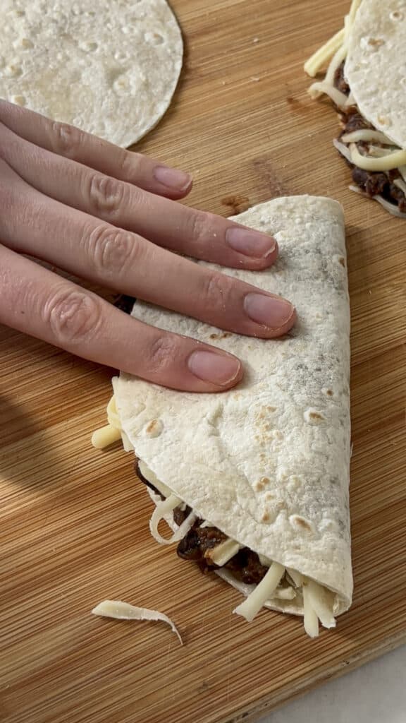 the taco folded in half over the black bean mixture and cheese, with a hand pressing the tortilla down