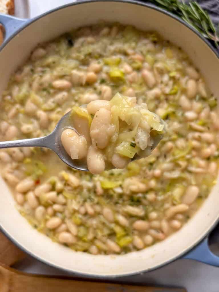 a spoonful of cheesy leeks and beans held above the pan
