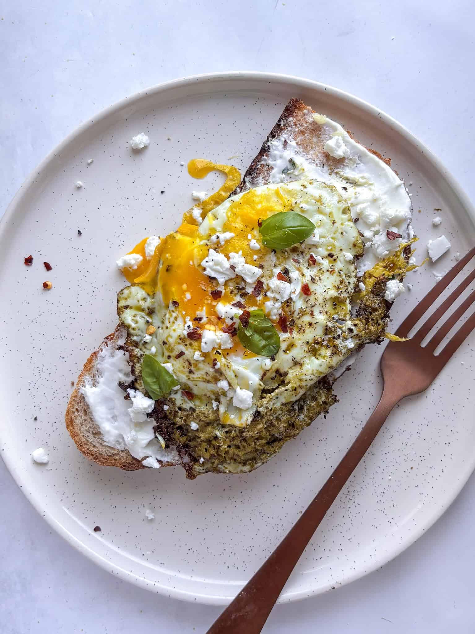 pesto eggs on sourdough on a white plate, with a fork on the side. Topped with chili flakes