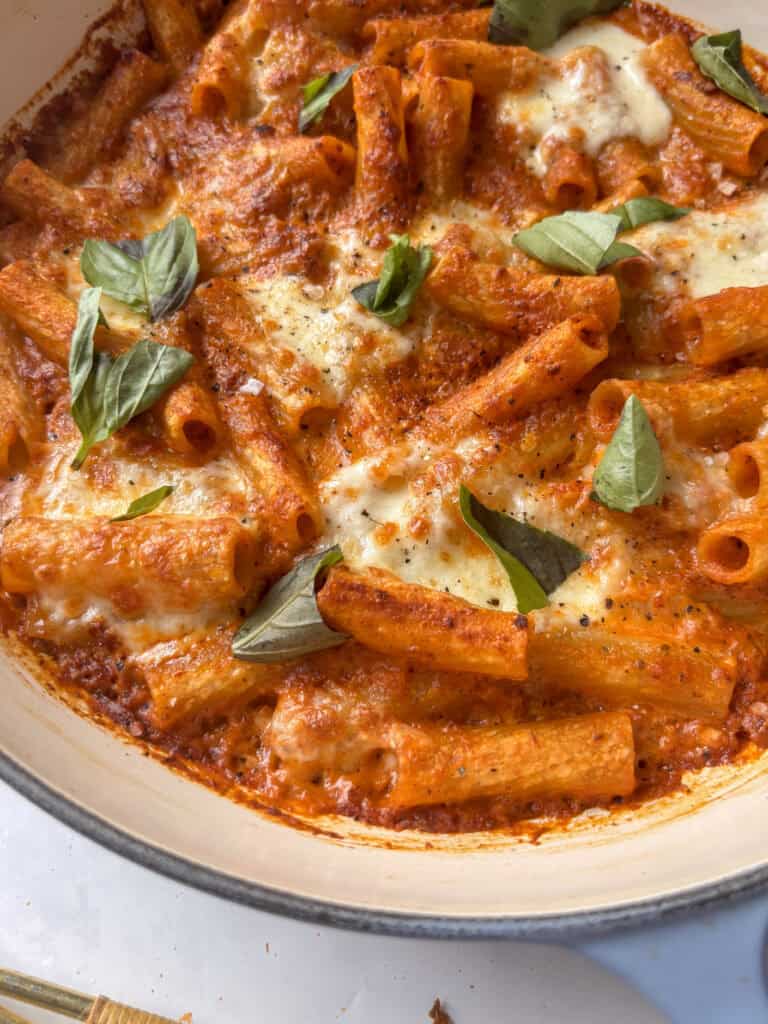 a casserole dish with creamy sun-dried tomato pasta topped with mozzarella and basil