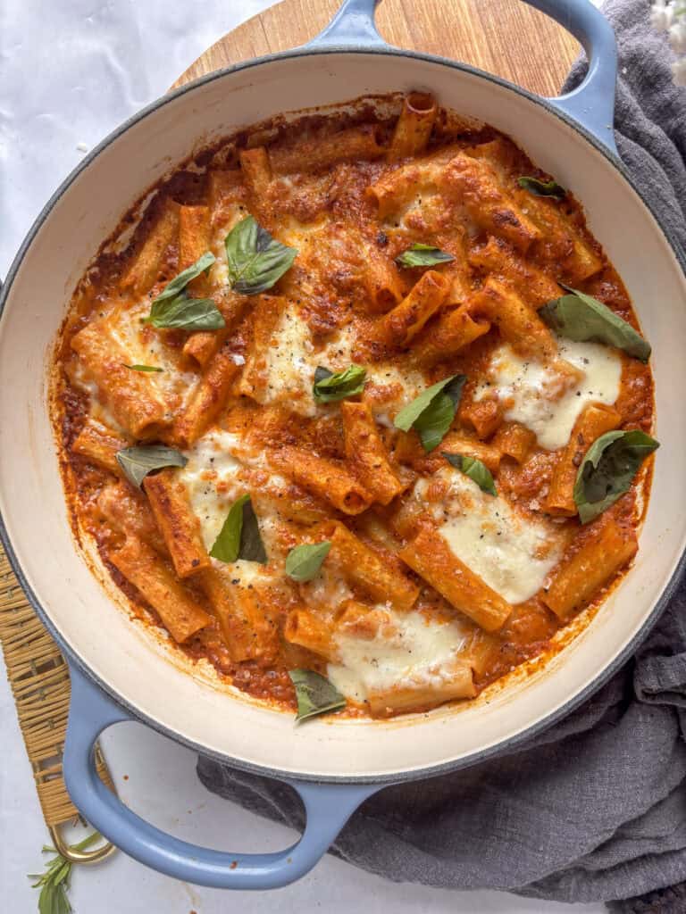 a casserole dish with creamy sun-dried tomato pasta topped with mozzarella and basil