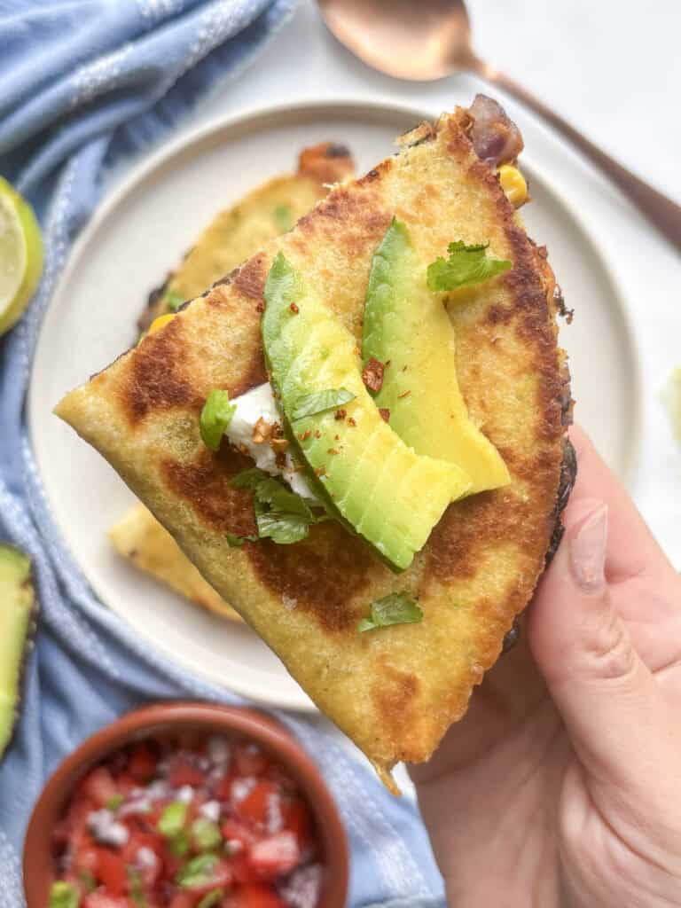 a crispy black bean and sweet potato quesadilla, topped with sliced avodado