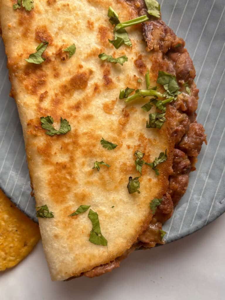 a close up of a crispy refried bean taco topped with cilantro