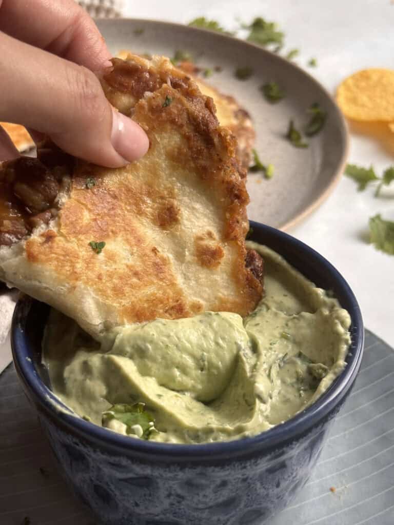 a refried bean taco being dipped into avocado lime crema