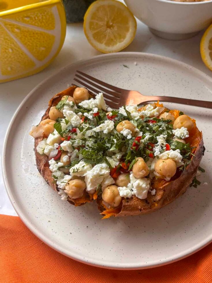 a loaded Greek sweet potato with chickpeas, feta, herbs, on a white plate