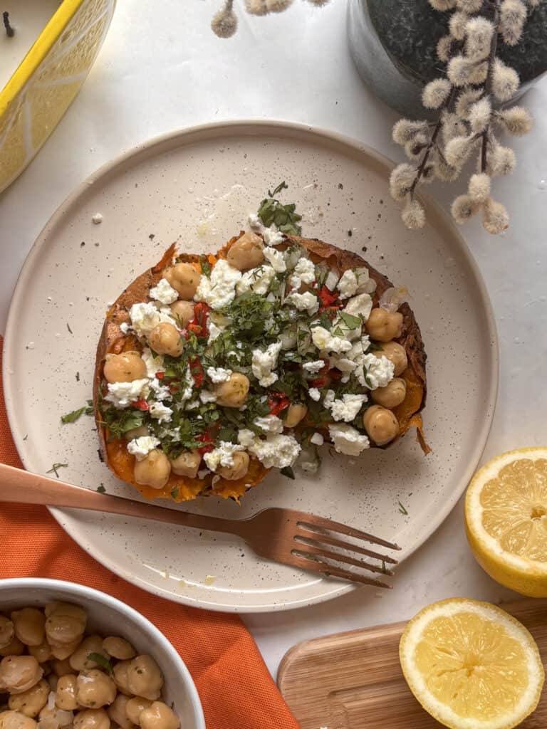 Greek stuffed sweet potato on a white plate loladed with chickpeas, feta, and fresh herbs