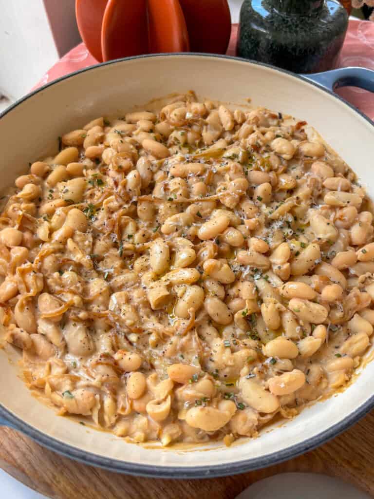 a casserole dish of caramelized onions and white beans topped with rosemary,