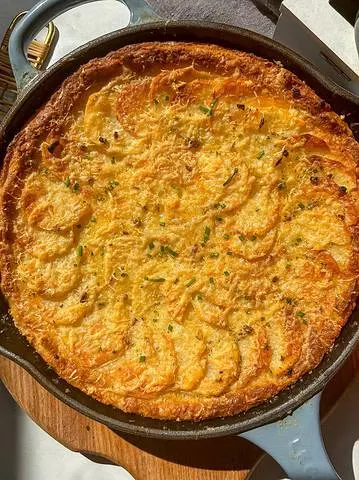 a skillet of cheesy mashed potatoes au gratin, topped with crispy cheesy thinly sliced potatoes