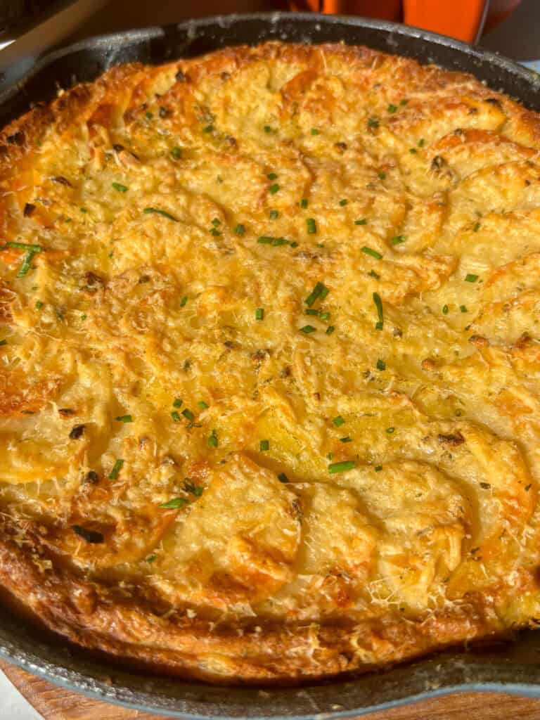 a close up shot of cheesy mashed potato au gratin in a cast iron skillet, topped with fresh chives