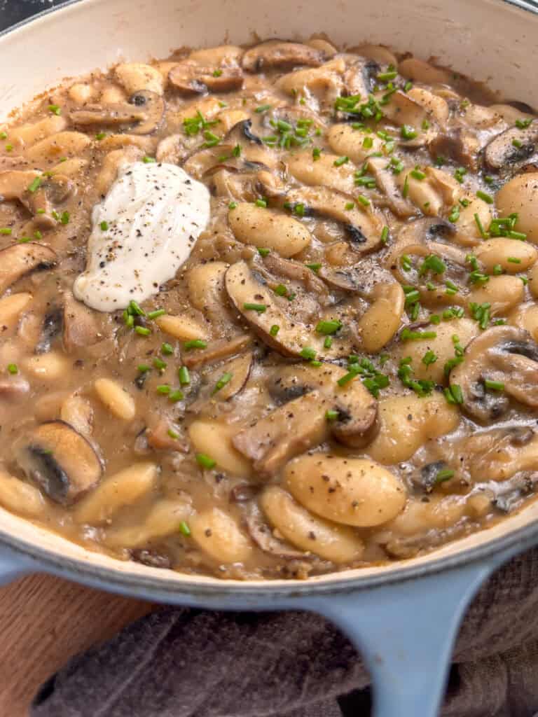 a casserole dish of sliced mushrooms and butter beans in a rich and creamy stroganoff sauce, topped with sour cream and parsely