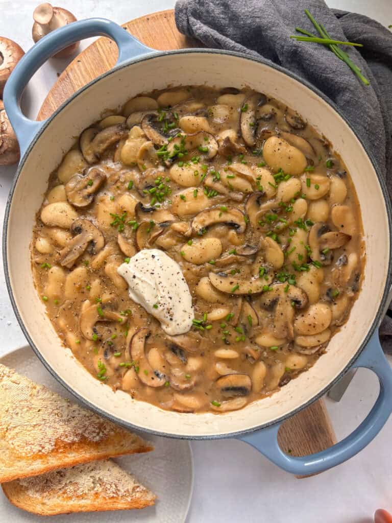 a casserole dish of sliced mushrooms and butter beans in a rich and creamy stroganoff sauce, topped with sour cream and parsely
