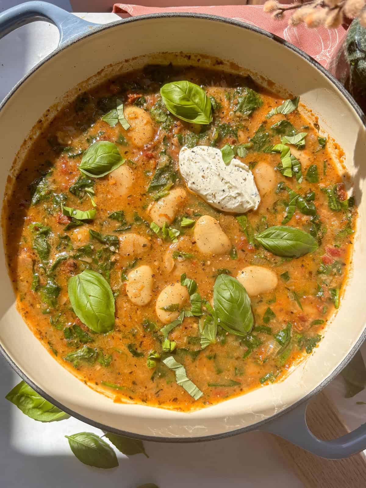 casserole dish of creamy tuscan butter beans topped with soft cheese and fresh basil
