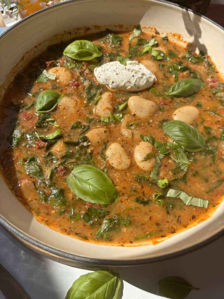casserole dish of creamy tuscan butter beans topped with soft cheese and fresh basil
