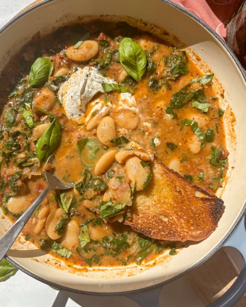 casserole dish of creamy tuscan butter beans topped with soft cheese and fresh basil and a slice of crusty sourdough