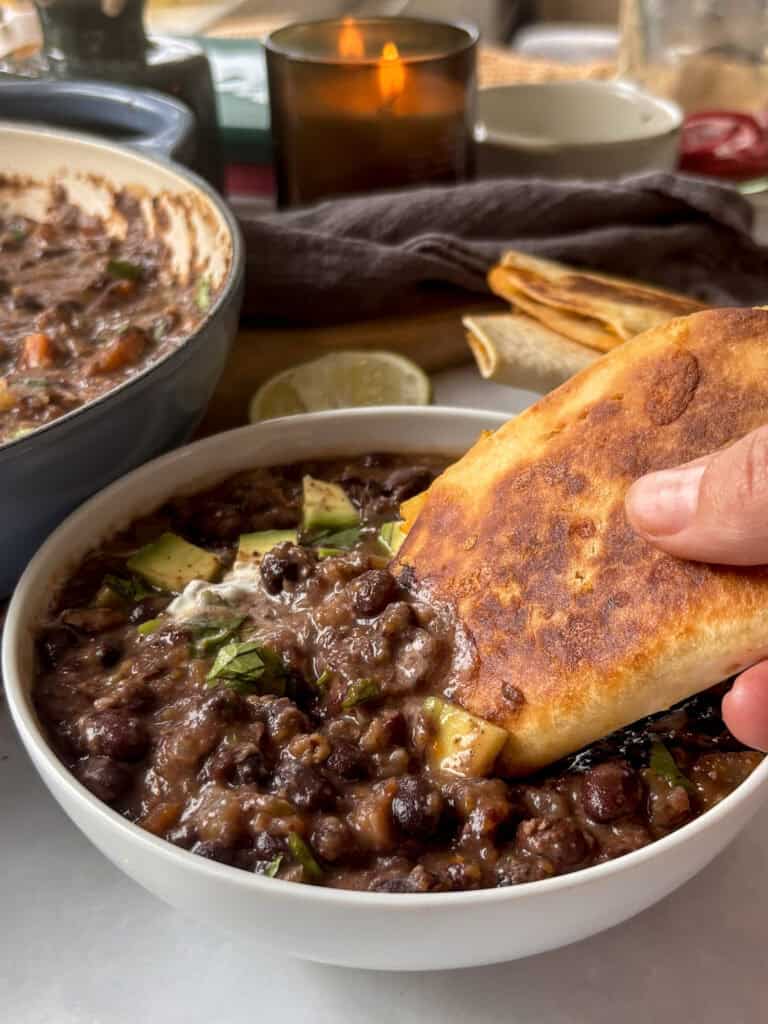 a bowl of black bean soup with a potato taco being dipped into it