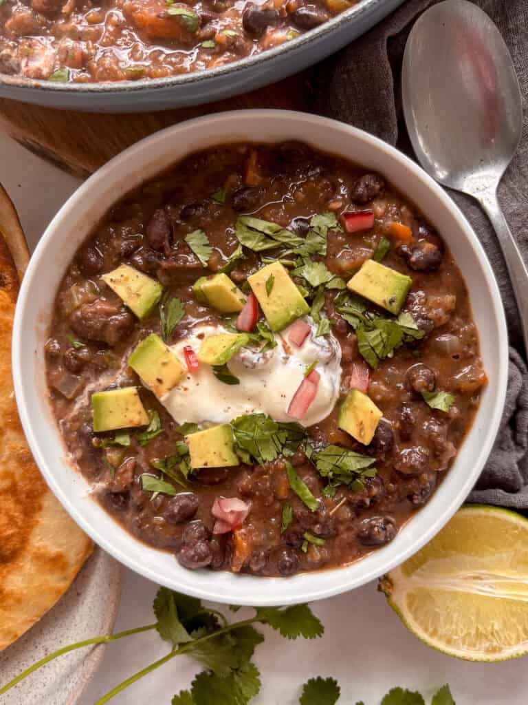 a small white bowl of black bean soup topped with sour cream, avocado, and cilantro