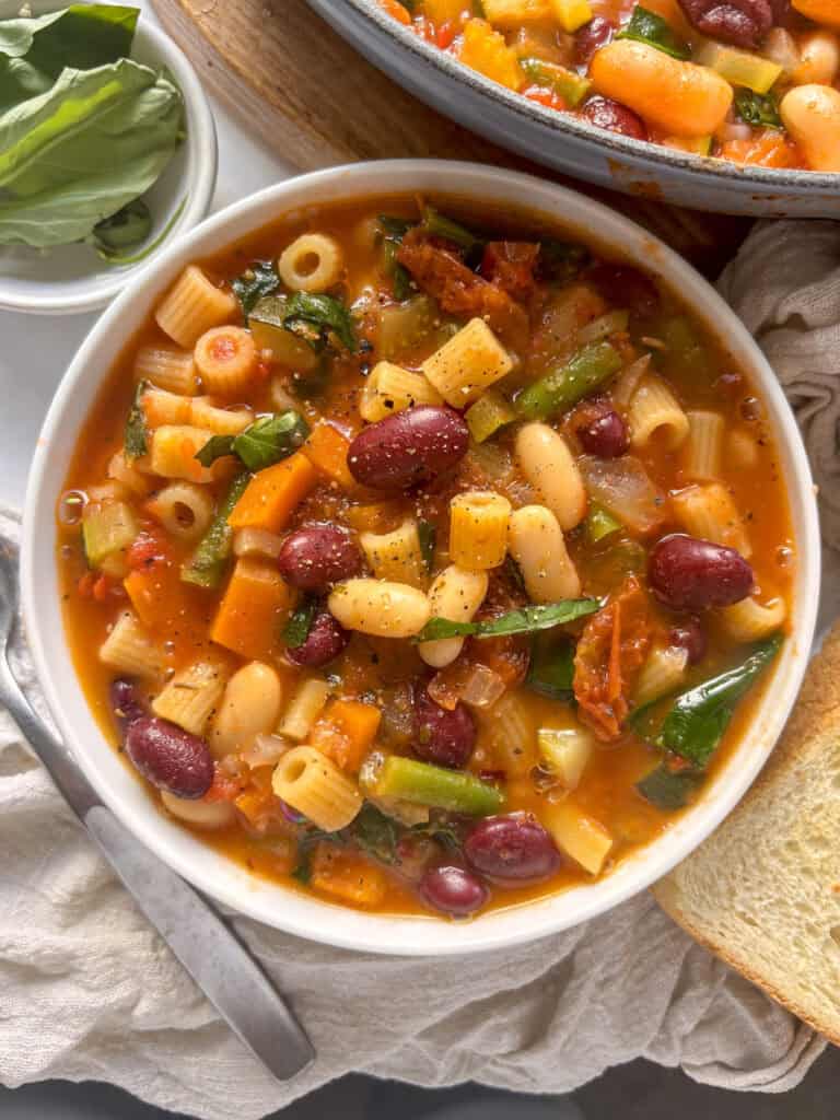 a serving bowl of minestrone soup, with a slice of crusty bread just off to the side