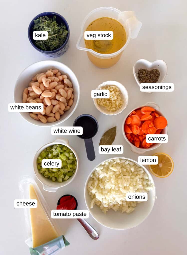 white bean soup ingredients shot: kale, vegetable stock, seasonings, garlic, white beans, white wine, bay leaf, carrots, lemon, onion, celery, tomato paste, cheese