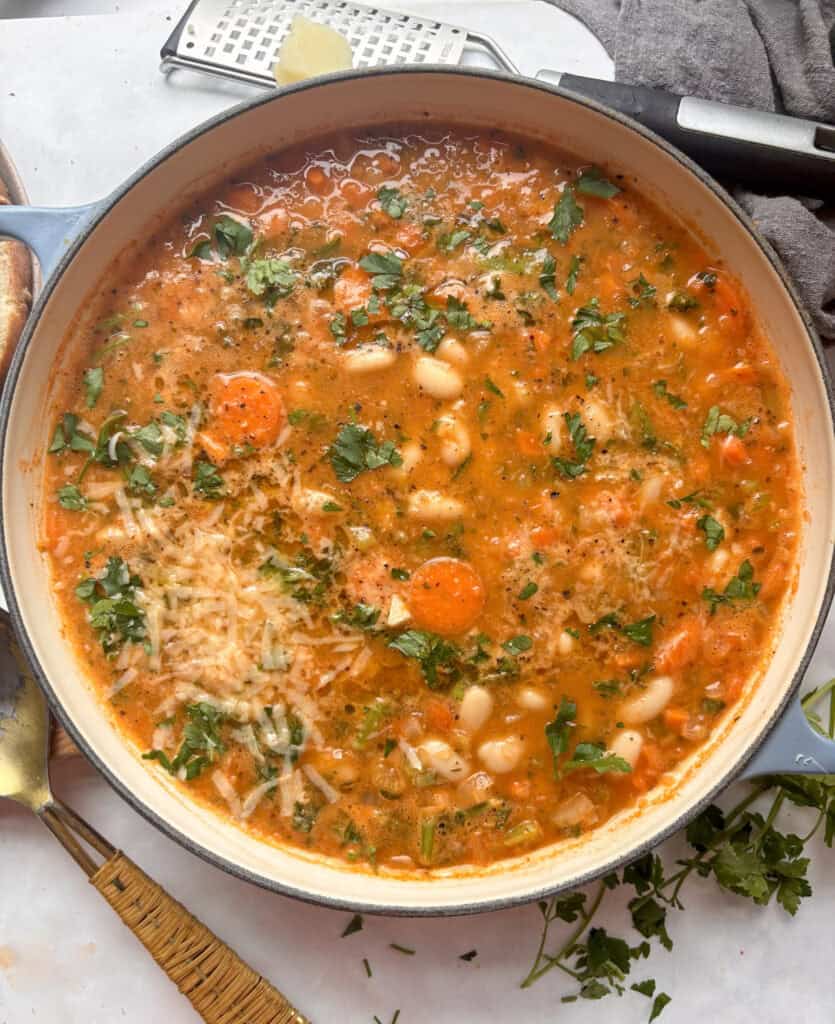 casserole dish of cozy white bean soup topped with parsley, cheese, and seasonings