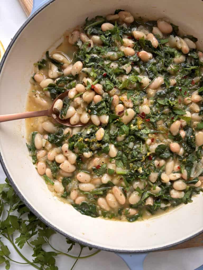 a pan of greens and beans topped with pepper flakes and lemon zest