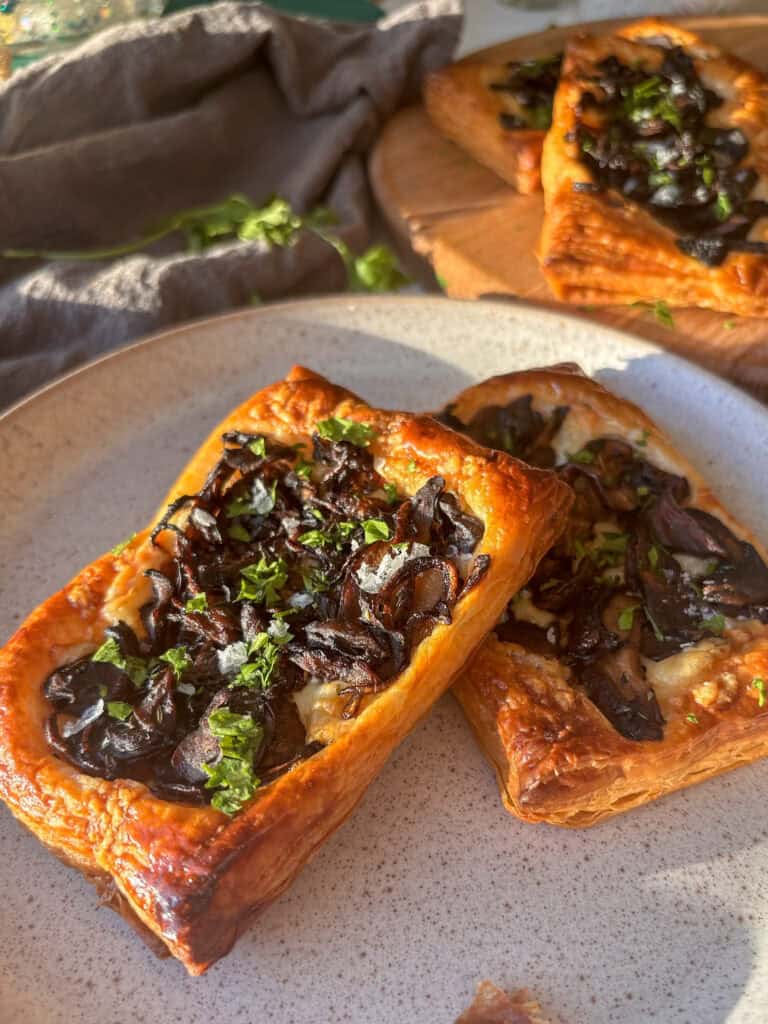 cheesy mushroom puff pastry tarts on a plate, topped with parsley and flaky salt