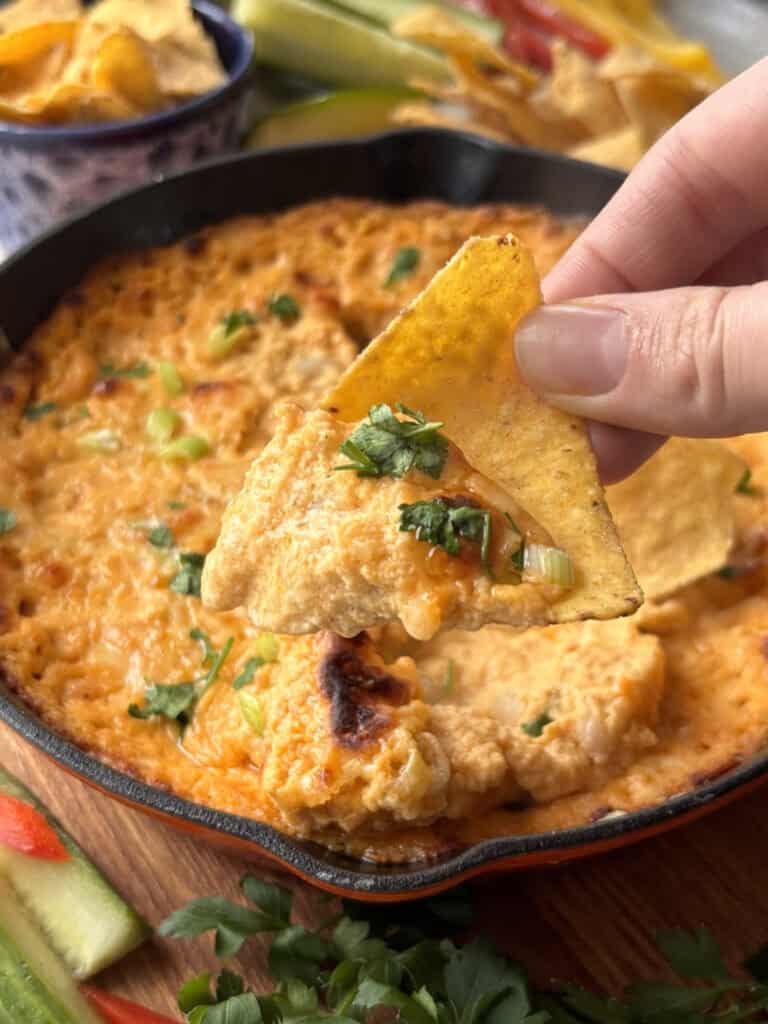 buffalo white bean dip on a tortilla chip, with the remaining dip in the background