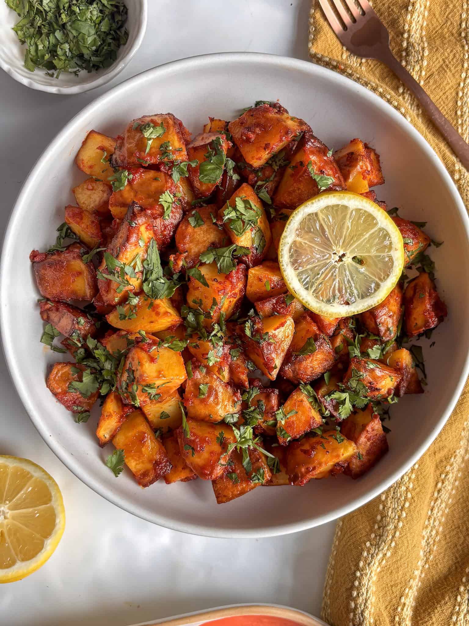 batata harra - spicy Lebanese potatoes - in a white bowl and topped with fresh cilantro and a slice of lemon.