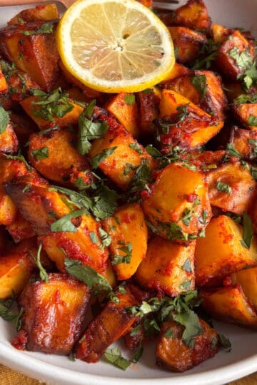 spicy lebanese potatoes - batata harra - piled into a bowl and topped with chopped fresh herbs and sliced lemon