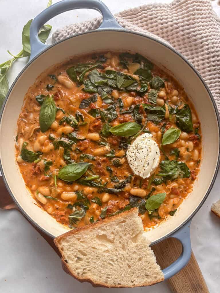 a skillet pan of creamy tuscan white beans with sun-dried tomatoes a, spinach, and basil.