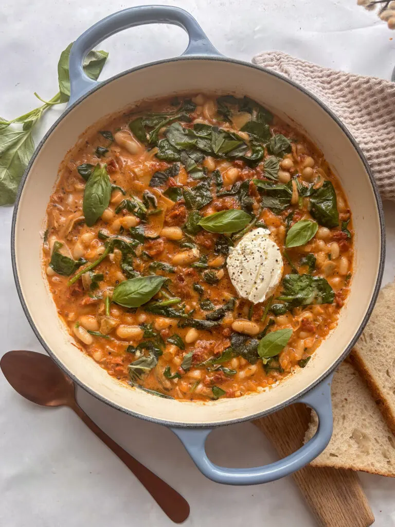a skillet pan of creamy tuscan white beans with sun-dried tomatoes a, spinach, and basil.