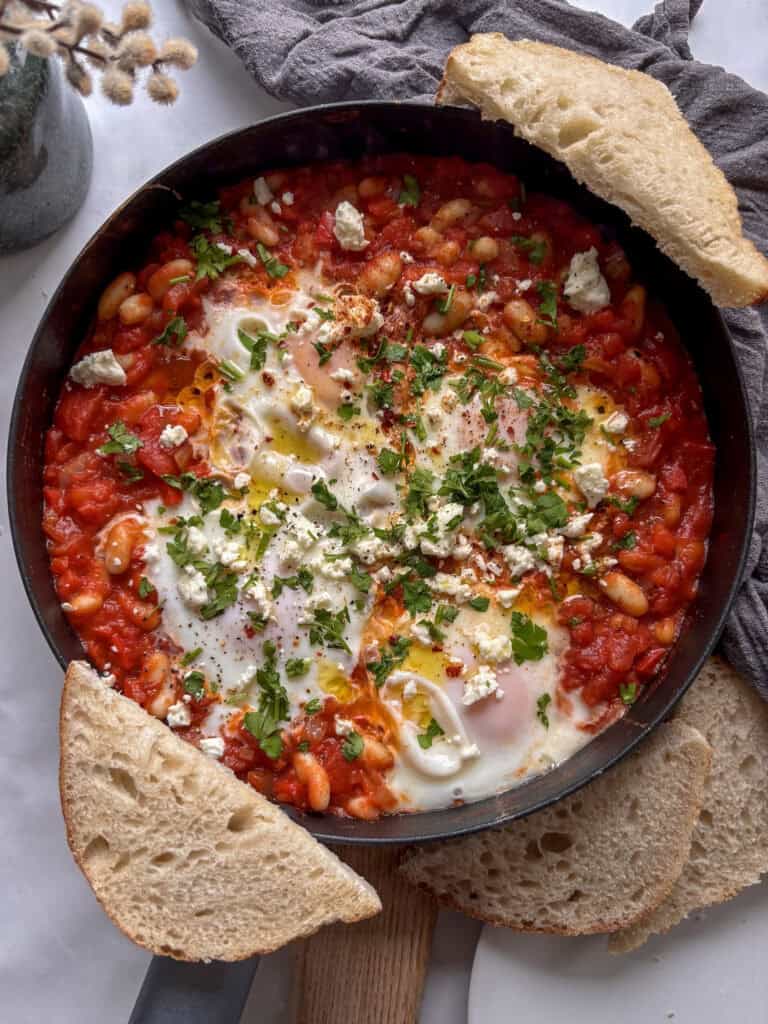 a skillet of white bean shakshuka topped with feta and parsley