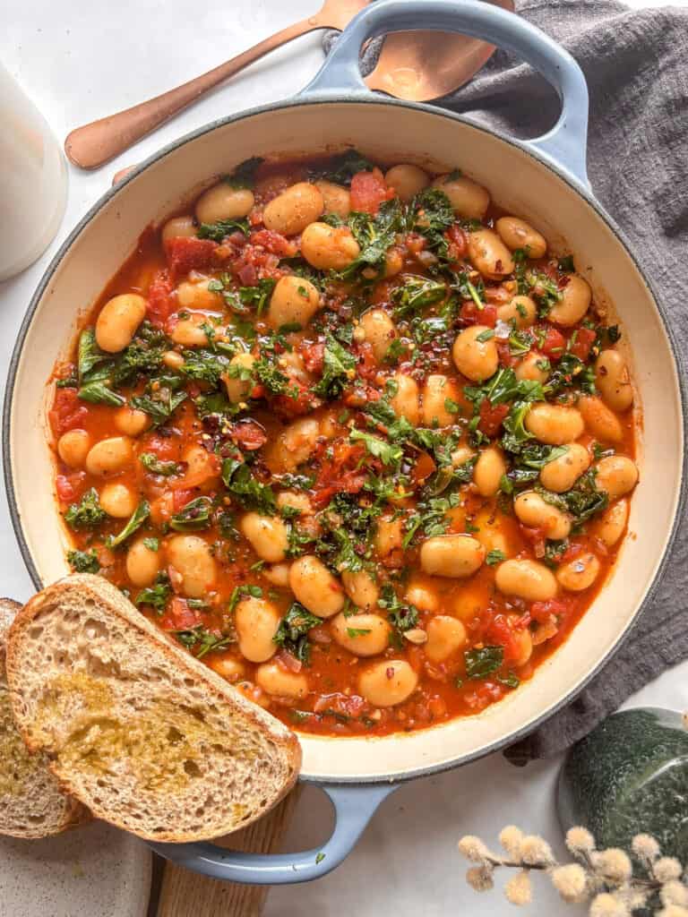 a large pan of butter bean and kale stew with some sourdough bread on the side
