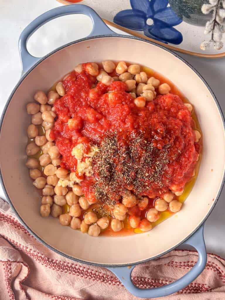 a casserole pan with oil, chickpeas, tomatoes, garlic, and spices added