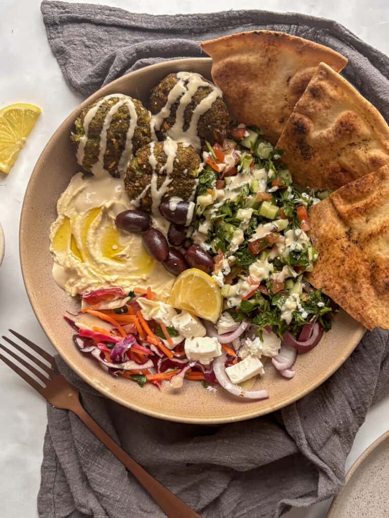 an overhead view of a vibrant falafel salad - with falafels, pickled cabbage, feta, pita chips, shirazi salad, lemon, hummus, and tahini sauce