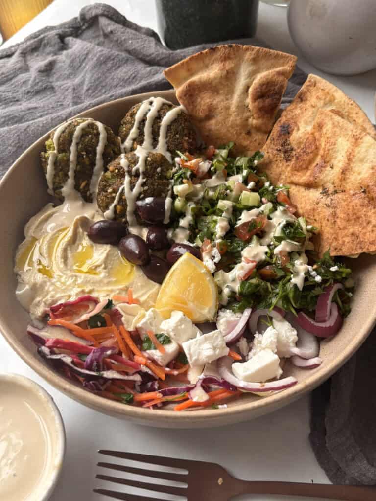 a falafel salad bowl with Shirazi salad, feta, pickled cabbage, falafels, hummus, pita chips, kalamata olives, and a tahini sauce