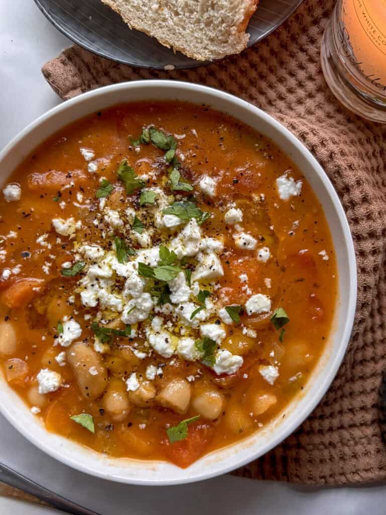 Greek bean soup - fasolada - in a white bowl topped with crumbled feta and extra virgin olive oil