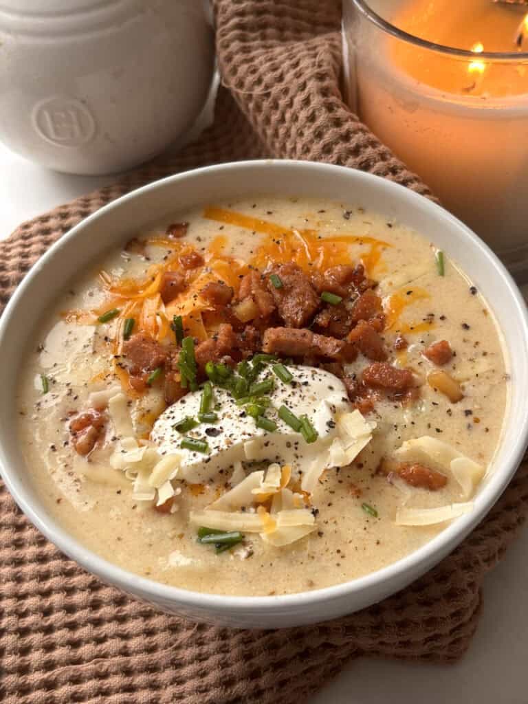 loadd baked potato soup in a white bowl with vegan bacon bits, sour cream, cheese, chives