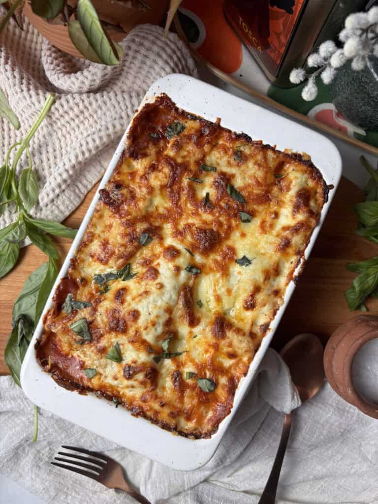 the dish of roasted vegetable lasagna with a golden cheesy topping and fresh basil