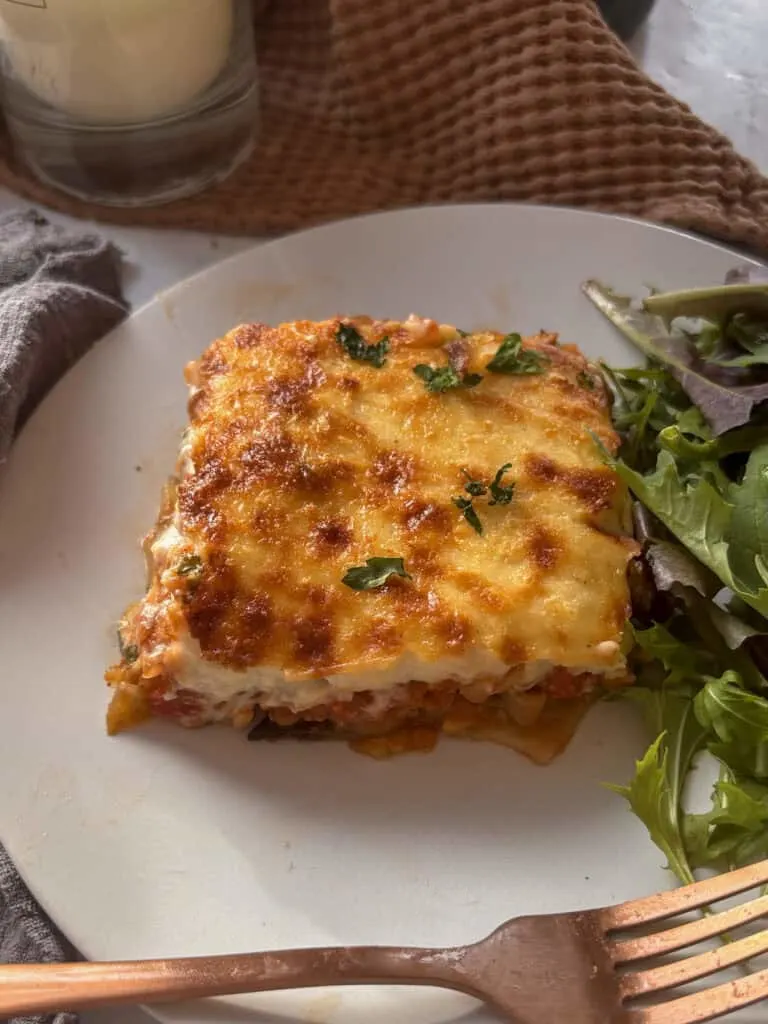 a slice of vegetarian moussaka on a white plate with a side salad next to it
