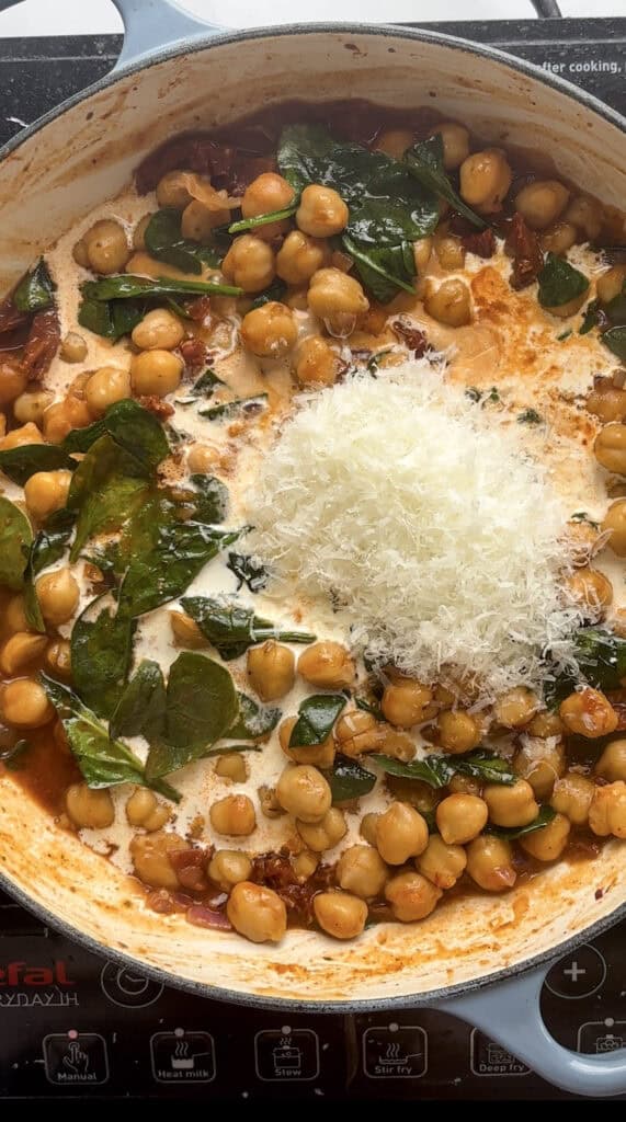 A scattering of hard cheese (Pecorino in this case) being tipped into the cassserole pan of Marry Me Chickpeas