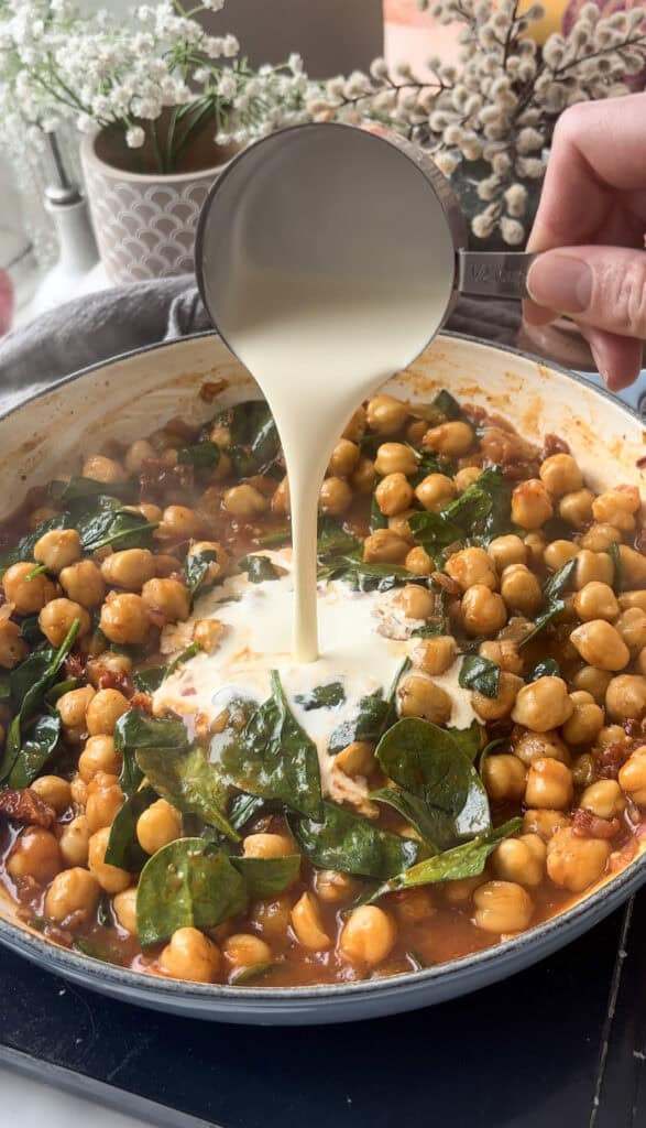 Heavy cream being poured into the pan of Marry Me Chickpeas