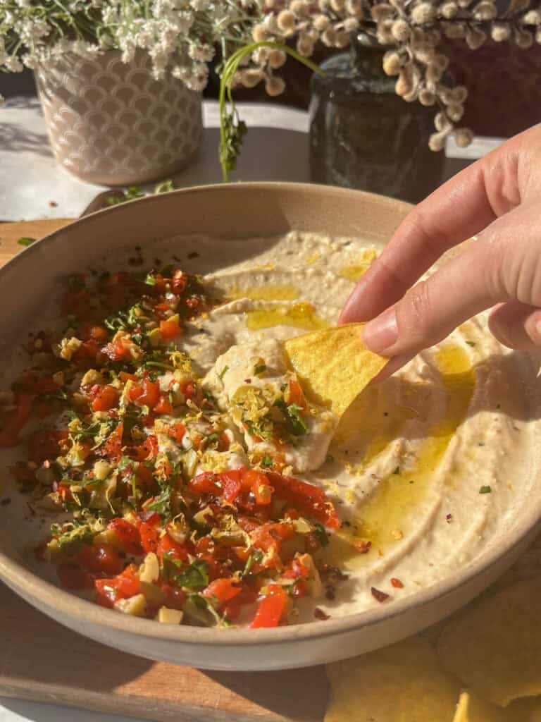 a tortilla chip being dipped into the white bean dip