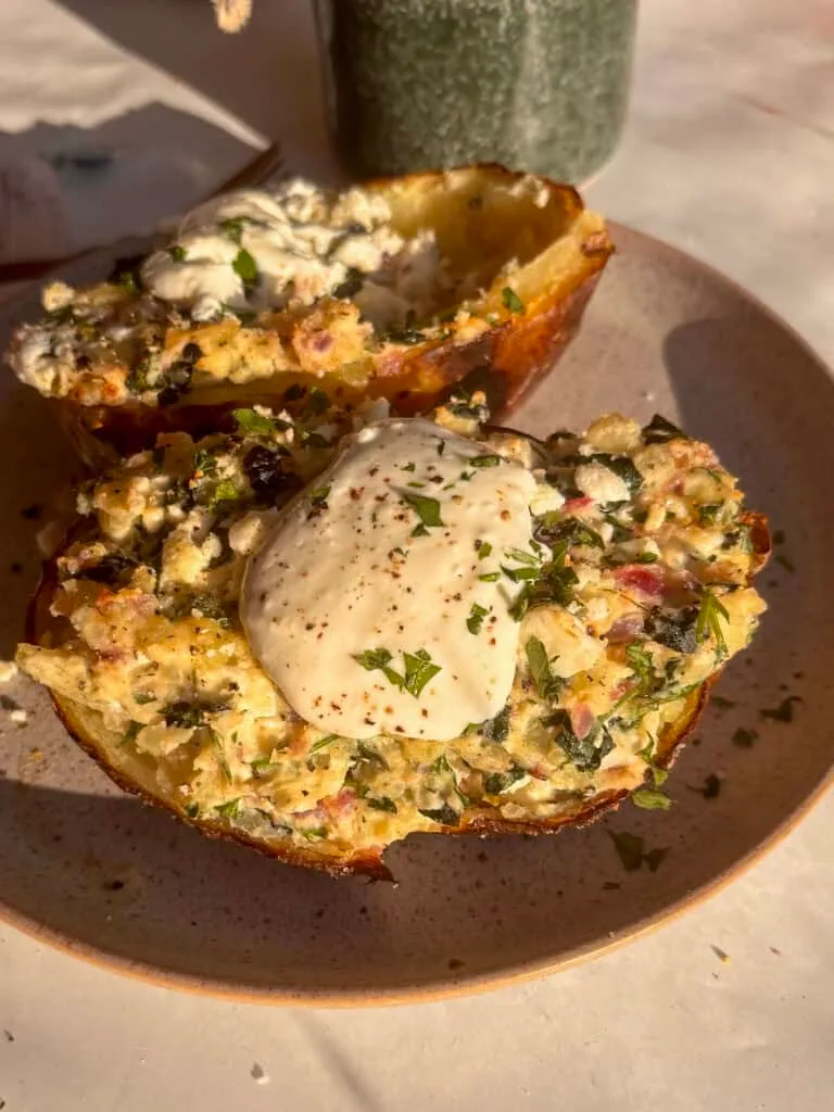 a loaded spanakopita potato with feta and onion and spinach, topped with tzatziki and parsley