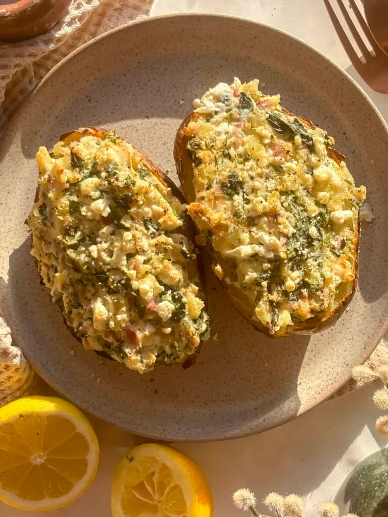two loaded spanakopita potatoes on a small serving plate, loaded with feta and spinach