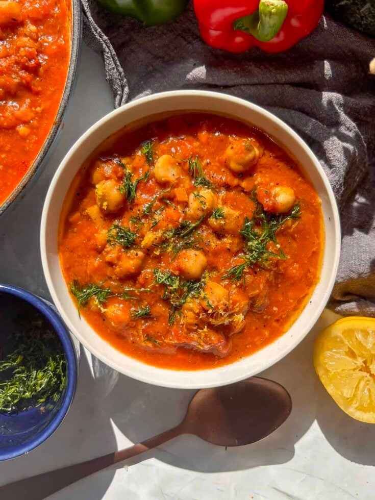 a white bowl of chickpea soup topped with fresh dill