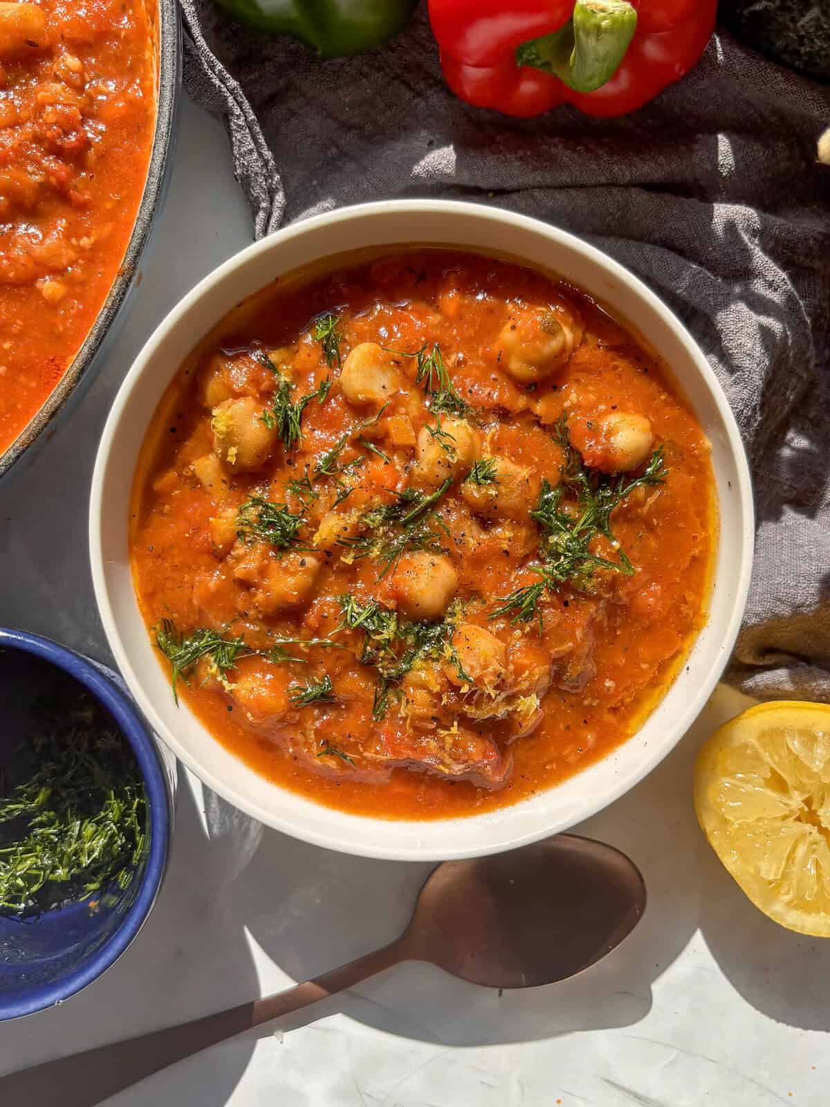 a white bowl of chickpea soup topped with fresh dill